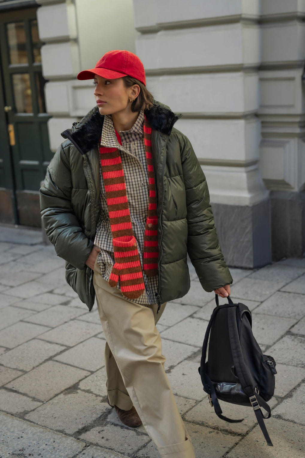 Striped knitted scarf mittens worn with a green puffer jacket, checked shirt and red cap in an urban setting.