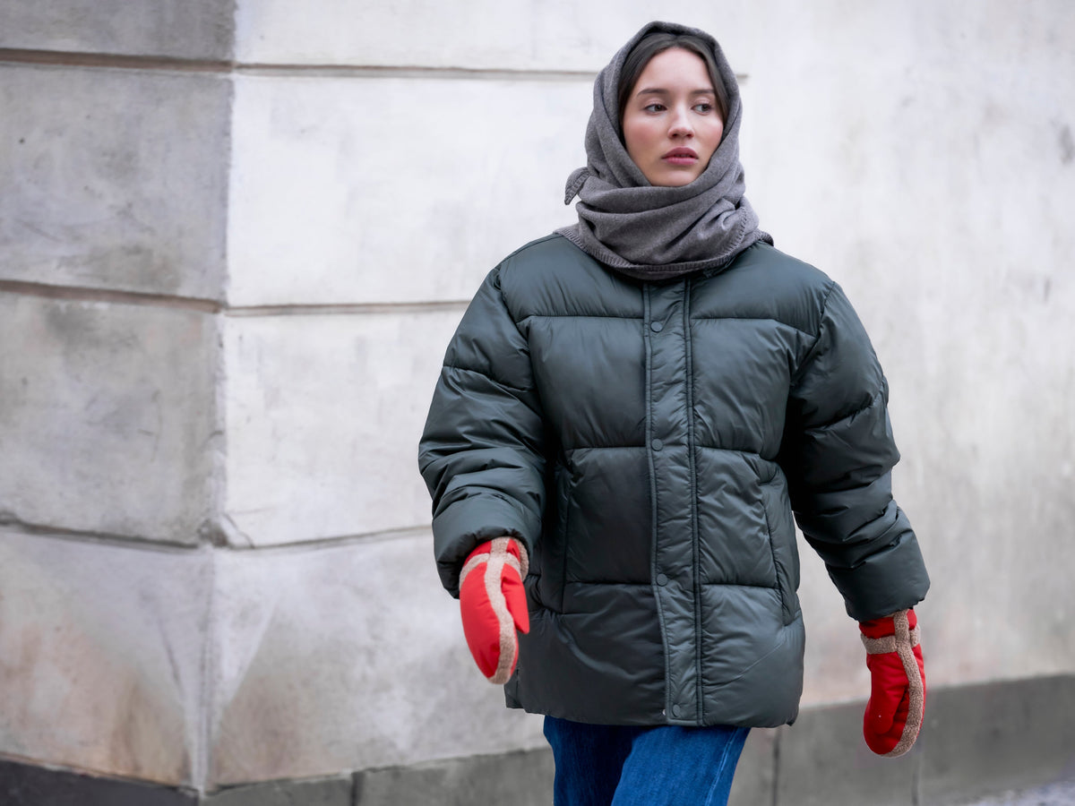 Woman wearing red mittens, a padded jacket, and a scarf while walking in an urban setting.