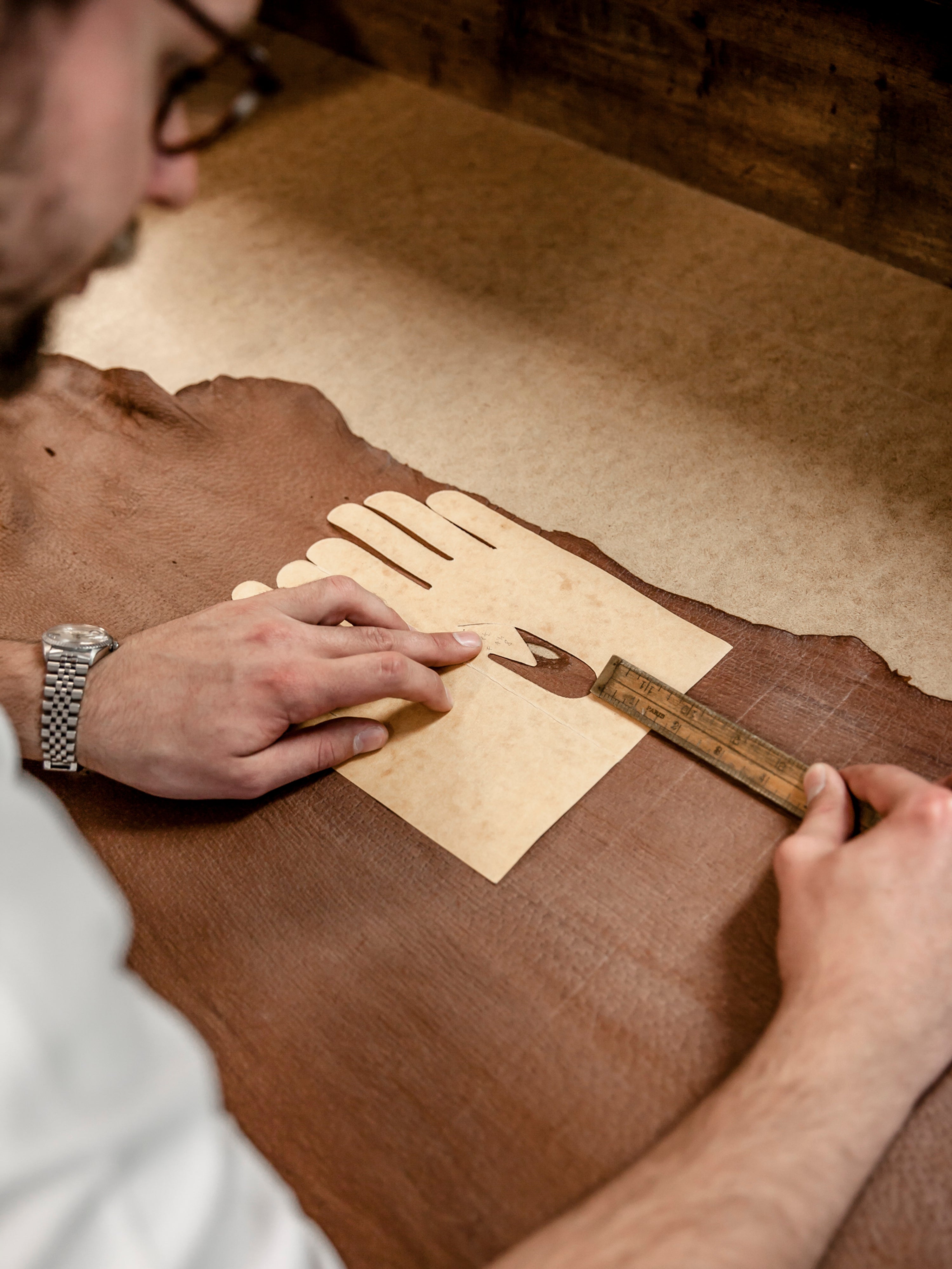 Craftsman laying out a cutting pattern on a leather hide, measuring with a brass ruler